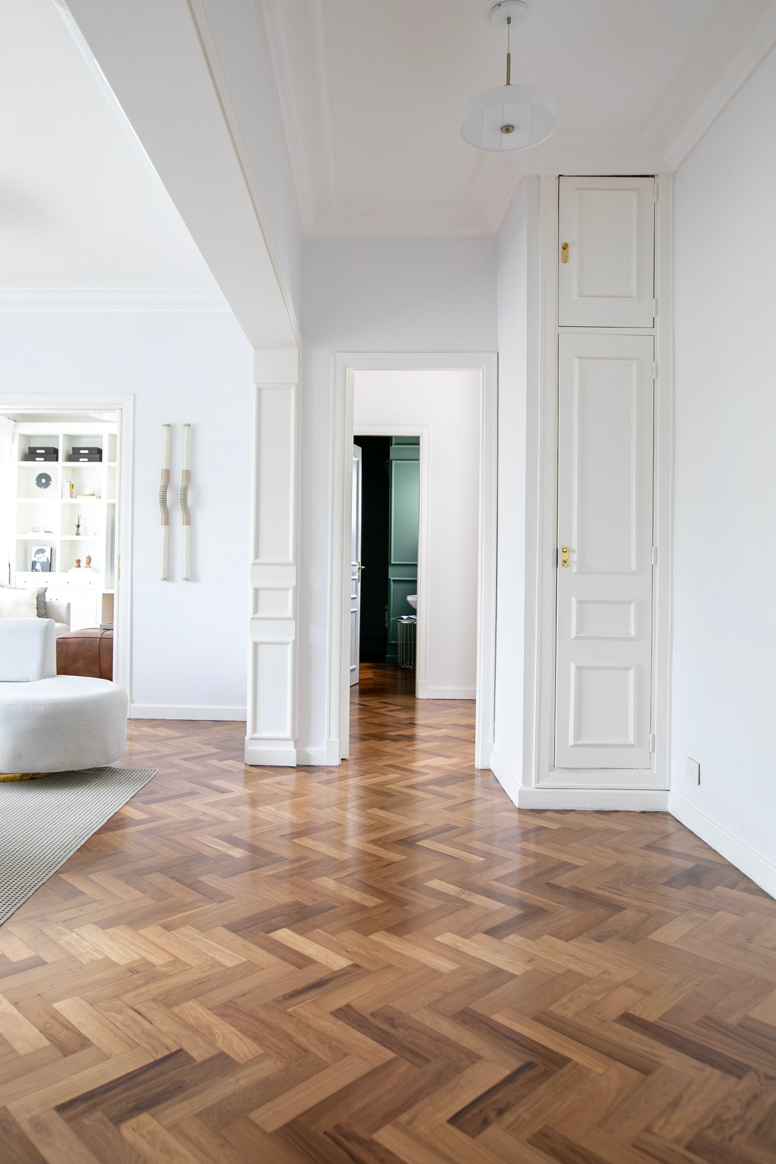 Corredor com piso de madeira espinha de peixe e armário embutido branco — projeto Lacroze, por Estudio Losa, em Belgrano
